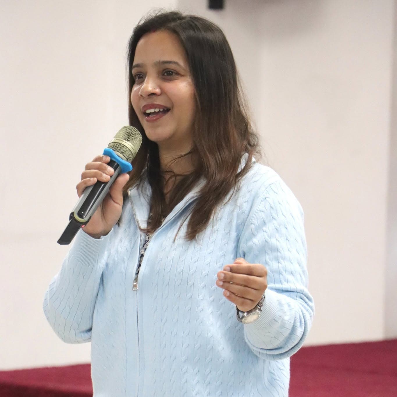 A woman smiling as she speaks into a microphone while addressing an audience.