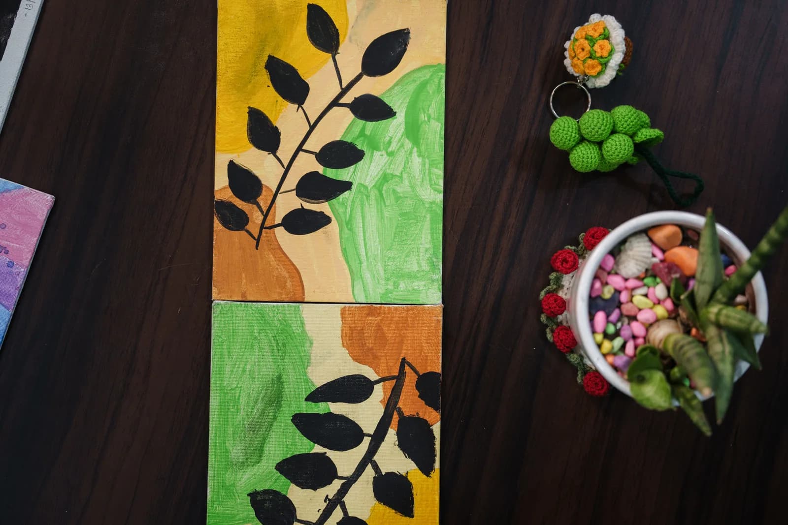 Two leaf paintings with black branches on yellow, orange and green backgrounds.