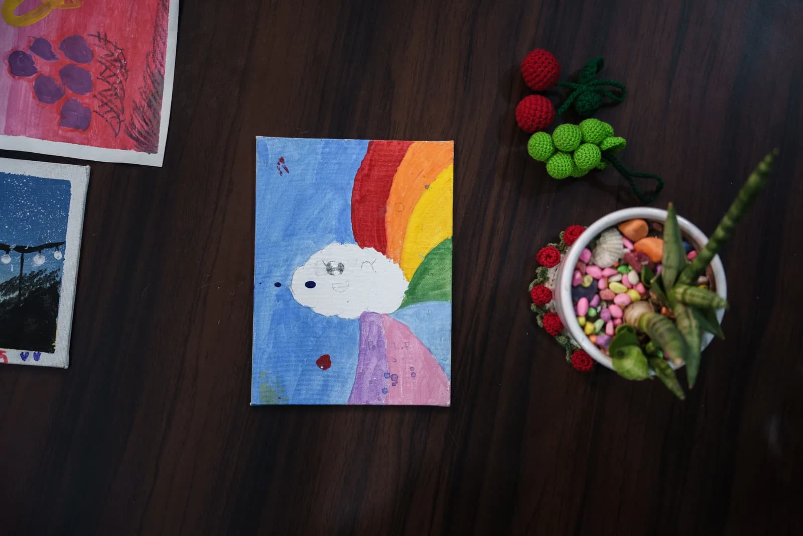 A colourful cloud and rainbow painting displayed on a wooden table.