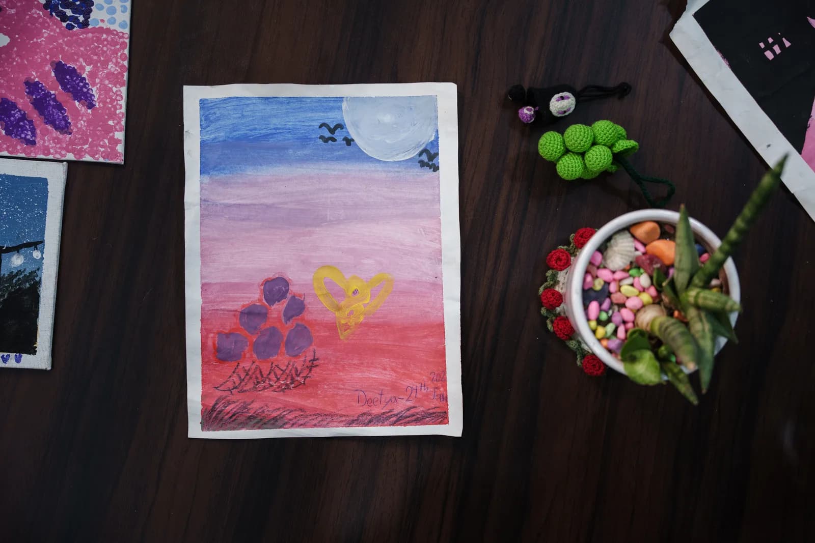 A blue, pink and red sunset painting with small figures holding a heart.