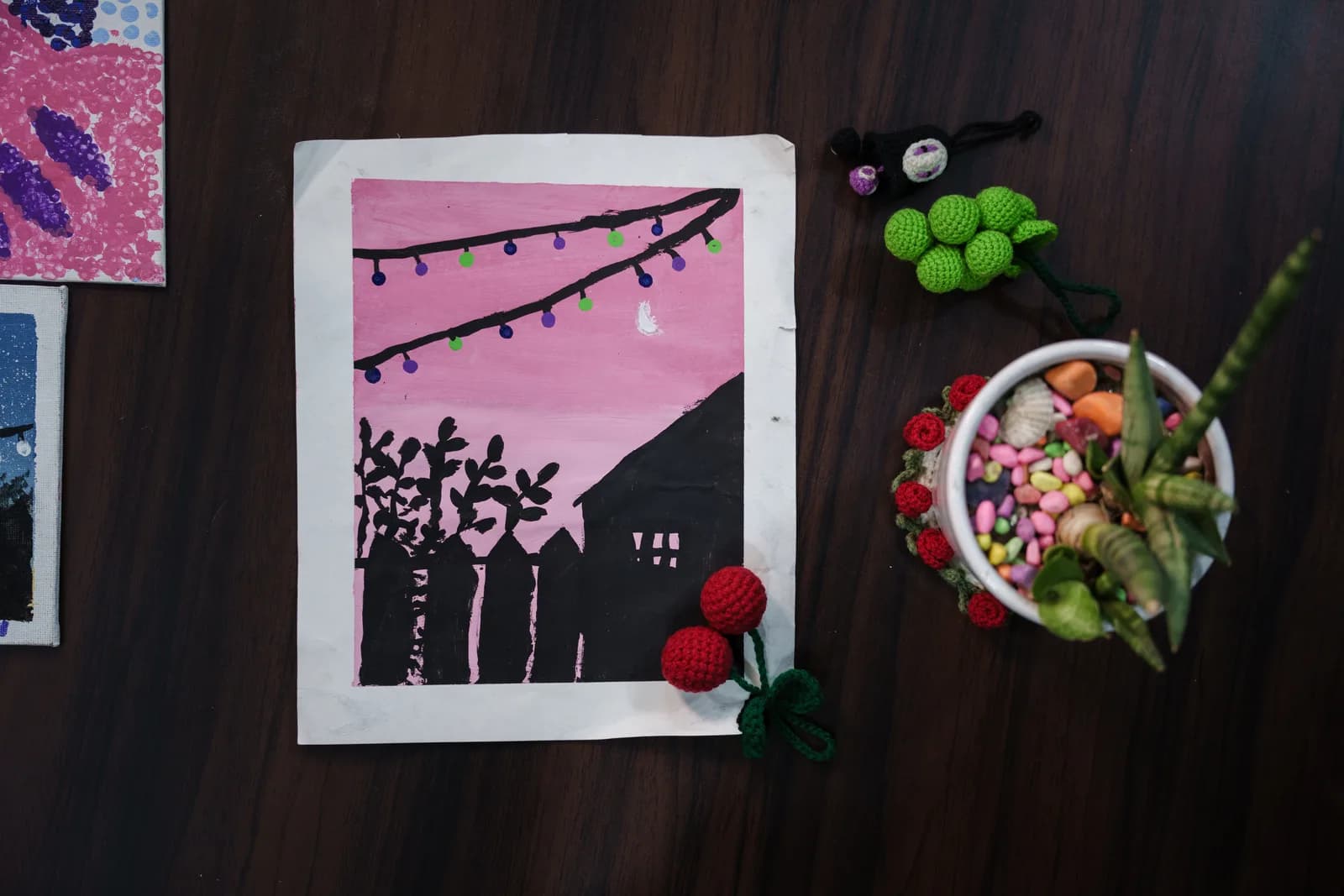 A pink night sky painting with a crescent moon, string lights and tree silhouettes.