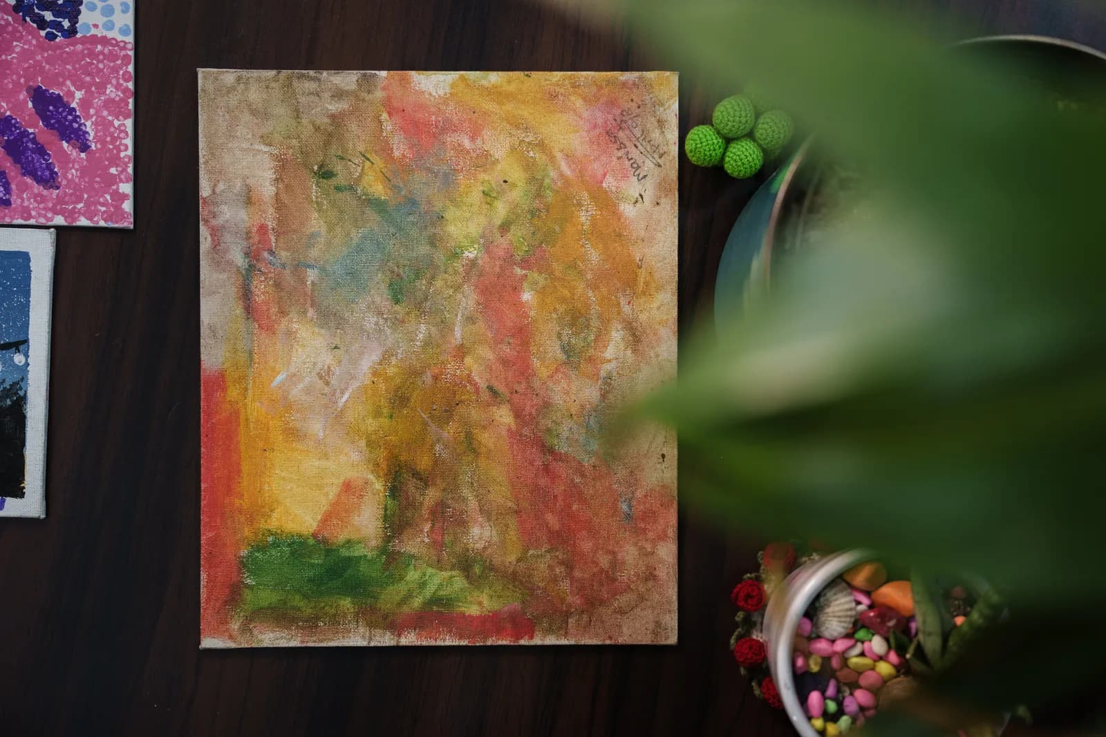 A colourful abstract painting photographed beside small green ornaments.