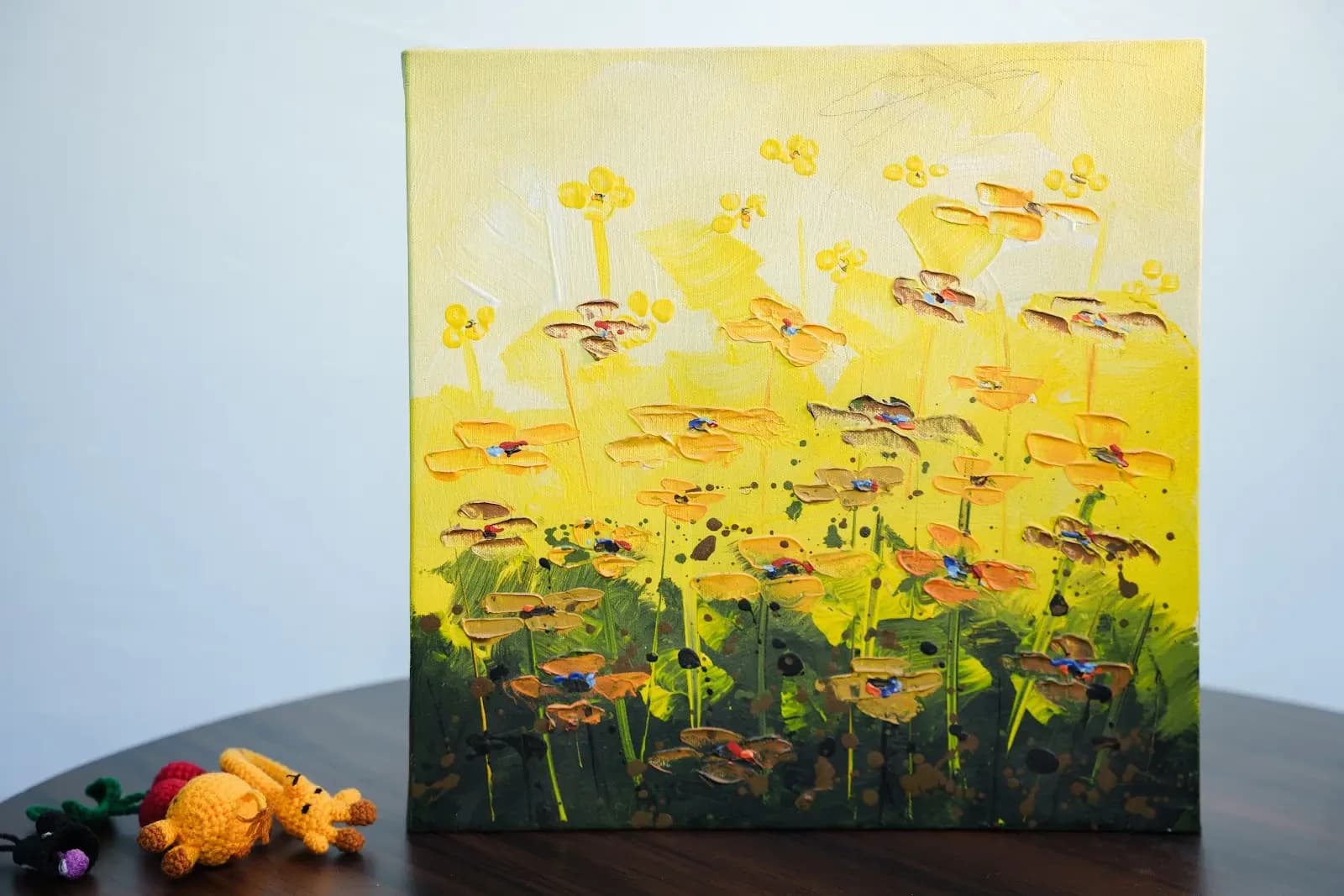 A painted canvas of bright yellow flowers with dark centres on green stems, propped up on a table.